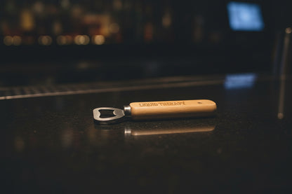 Wooden bottle opener with 'LIQUID THERAPY' engraving on a wooden surface