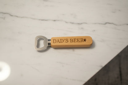 Bottle opener with 'DAD'S BEER' engraving on a wooden surface