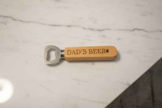 Bottle opener with 'DAD'S BEER' engraving on a wooden surface